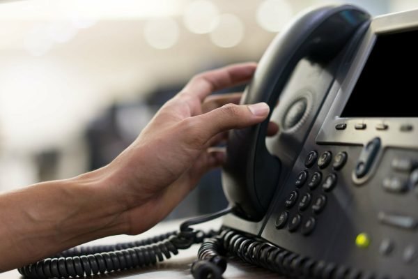 close up employee man hand touching handset of  telephone on desk for contact customer or receiving call , hotline  concept